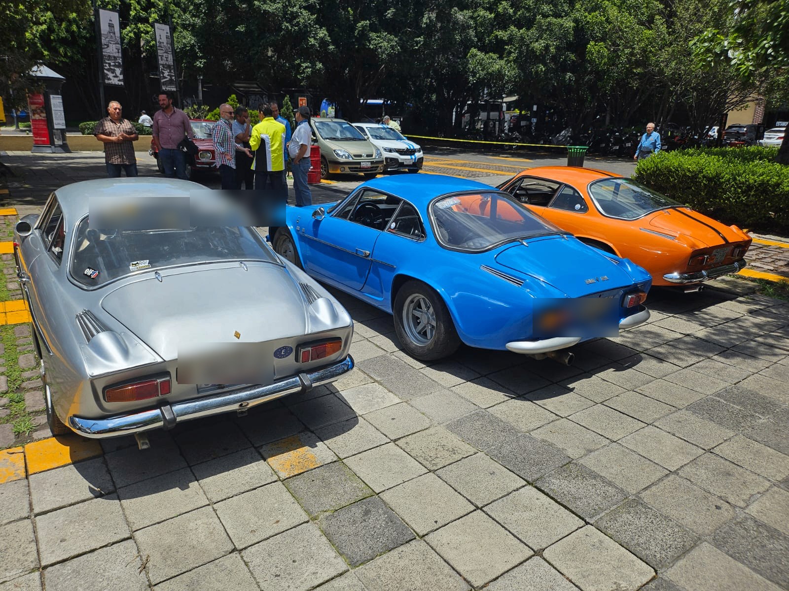 Tres Alpine clásicos plata, azul y naranja reunidos en el desayuno del 12 de julio de 2026, vistos desde la parte trasera con matrículas difuminadas