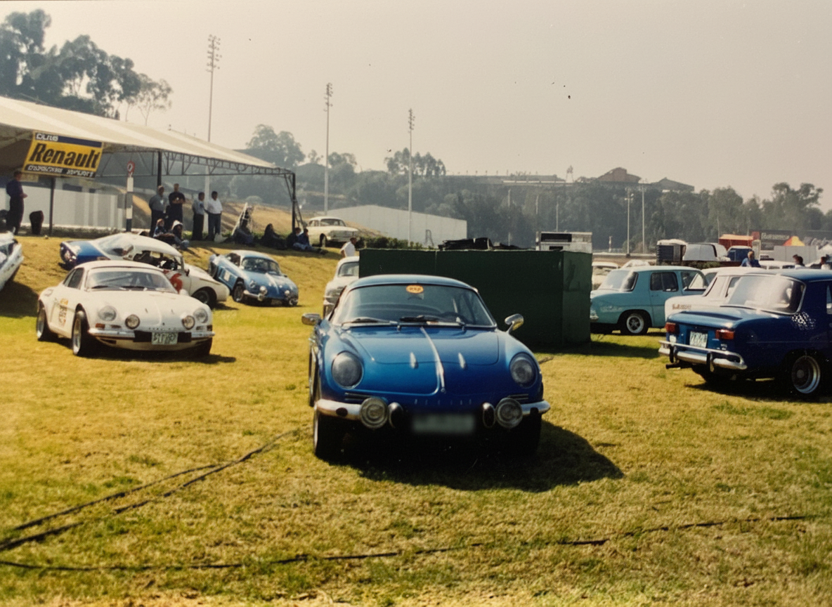 Alpine A110 azul y otros Alpines y Renault 8 en el paddock del Autódromo Hermanos Rodríguez con el stand del Club Renault Gordini Sport