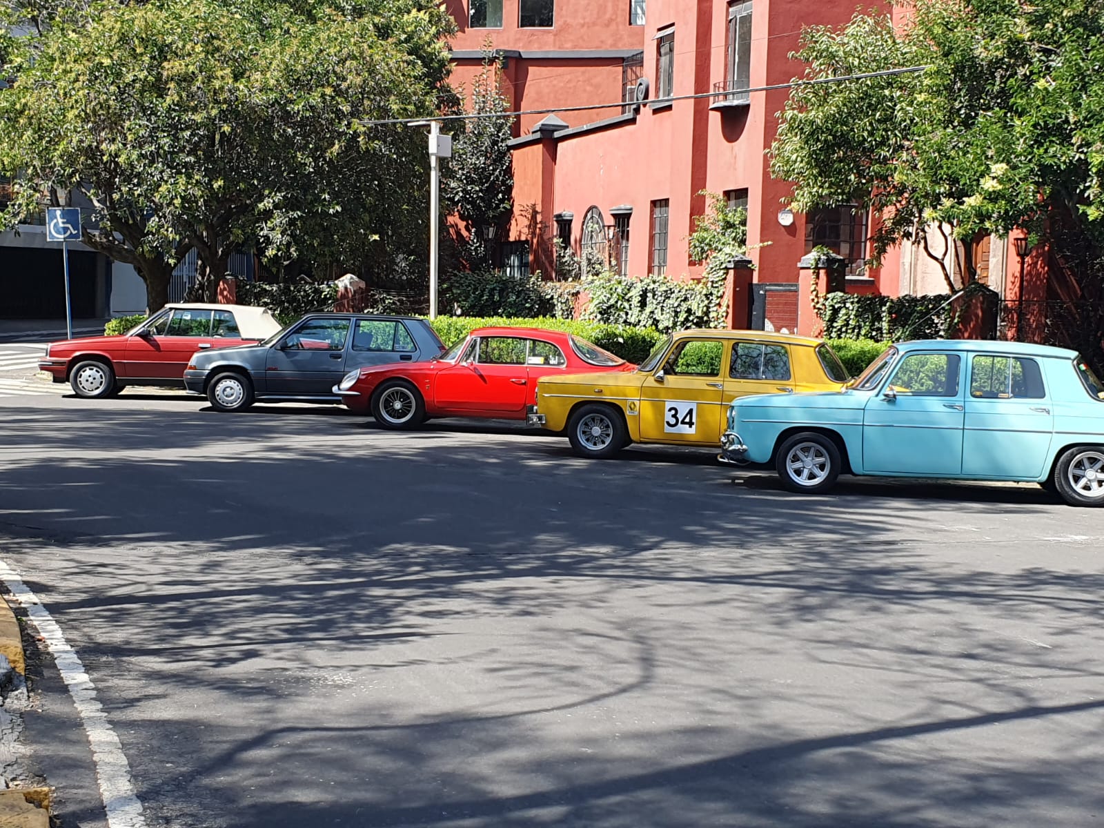 Renault clásicos rojo, gris, Alpine rojo, R8 amarillo #34 y R8 azul en calle colonial
