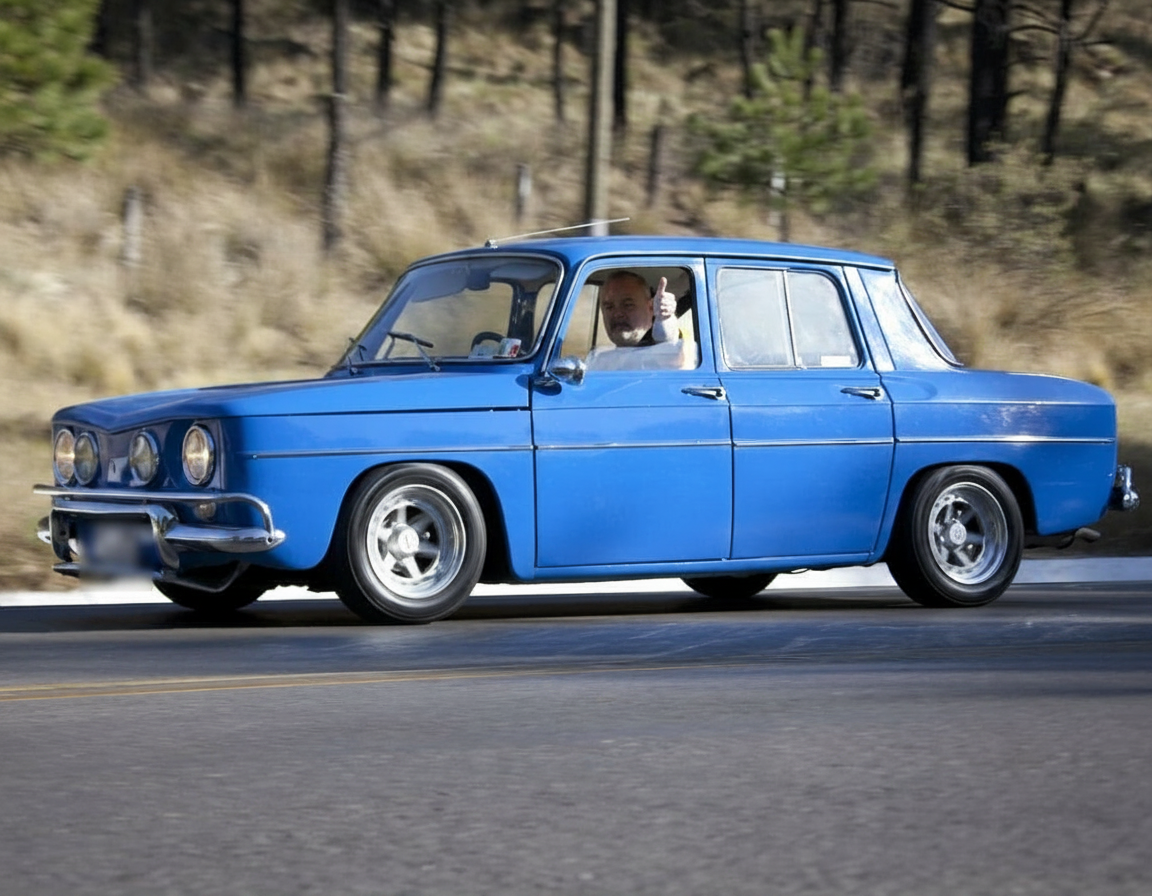 Renault 8 azul en carretera con conductor mostrando el pulgar arriba